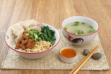 Mie ayam (noodles with chicken, meatballs, dumplings and vegetables) is a popular street food in Indonesia. Served in bowl on wooden table. Selective focus image, blurred background. Close up.
