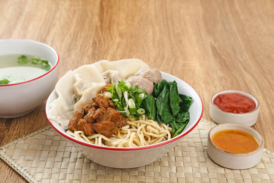 Mie ayam (noodles with chicken, meatballs, dumplings and vegetables) is a popular street food in Indonesia. Served in bowl on wooden table. Selective focus image, blurred background. Close up.

