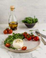 Front view of Italian cow milk cheese burrata with rucola and tomato cherry on plate over grey background