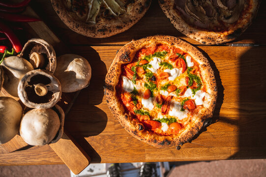 Wood fired artisanal pizza cooked in wood oven on rustic vintage chopping board served with fresh veg in summer sunshine with home made sauces and tasty ingredients vegetarian vegan pepperoni cheese