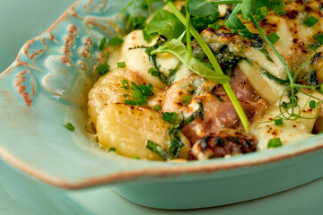 Baked potatoes in cream with cheese and bacon in a plate on a white tablecloth. Close-up