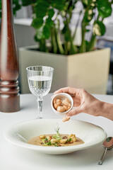 A woman's hand pours croutons into mushroom cream soup