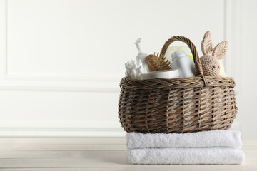 Wicker basket with different baby cosmetic products, accessories and toy on white wooden table....