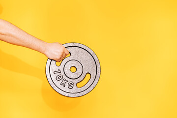 Hand holds ten-kilogram barbell dumbbell against yellow background.