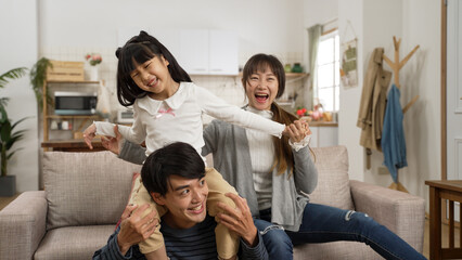 loving asian father giving his daughter piggyback ride on shoulders with mother’s support. the...