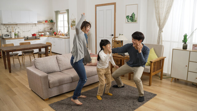full length shot happy Asian family of three having fun dancing together at home. they move their body to song in a cozy modern home interior with daylight