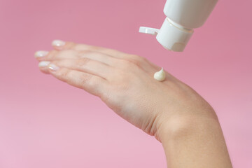 Young hands squeezing cream from tube on pink background. For beauty or medicine products