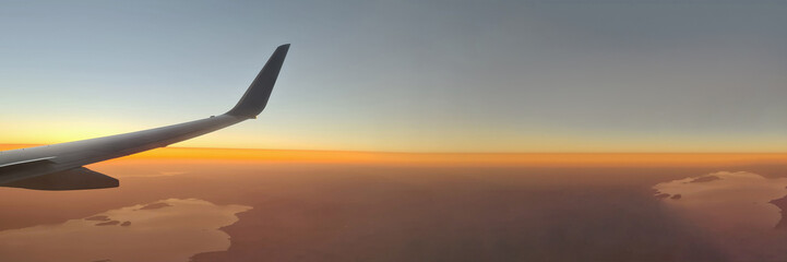 Obraz premium Closeup of airplane wing above ground at sunset background
