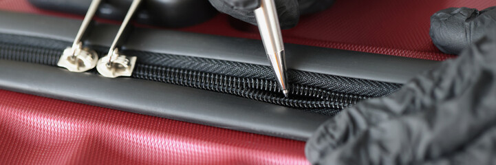 Thief in black gloves opening suitcase lock with ballpoint pen closeup