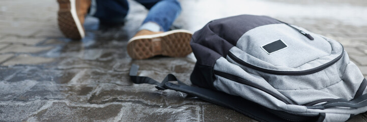 Backpack lying on slippery paving slabs near falling man closeup
