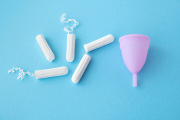 Menstrual cycle. Alternative means of hygiene and protection in critical days for women. Tampons and silicone menstrual cup on blue background. Selective focus. Copy space