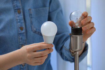 Woman changing incandescent light bulb for fluorescent one in lamp at home, closeup. Saving energy...