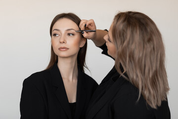 Professional attractive make-up artist tweezing eyebrows of young good-looking woman model. Make-up, advertisement.