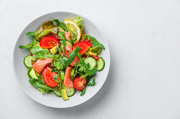 Salad with salmon and fresh vegetables on a light gray background.