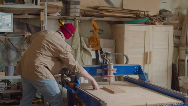Professional woodworker using computer while operating CNC machine in carpentry workshop