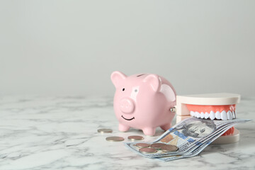 Educational dental typodont model, piggy bank and money on white marble table, space for text....