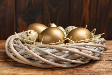 Golden and quail eggs in nest on wooden table, closeup