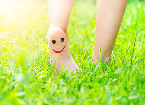 child's feet with a painted smile on the heel outdoors in the grass
