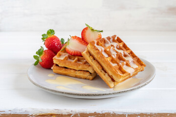 Waffles with fresh strawberries on gray plate over white wooden background.