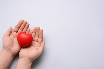 Man holding red decorative heart on light grey background, top view and space for text. Cardiology concept
