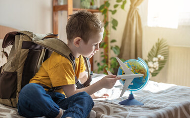 A child boy with backpack is playing with a toy airplane and a globe of the earth. Going on a journey towards adventure.
