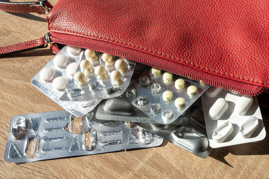 Blisters with antidepressants and pills lie on the table next to a red women's bag. Treatment of depression, stress, illness. Support for the human body with pills.