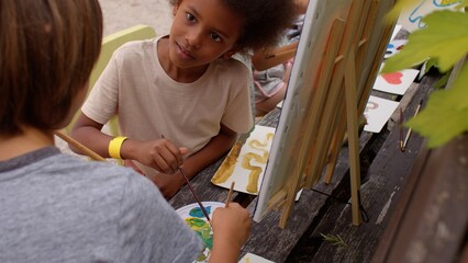 Painting workshop for kids in the art camp. Children paint with paints during the open air. A...