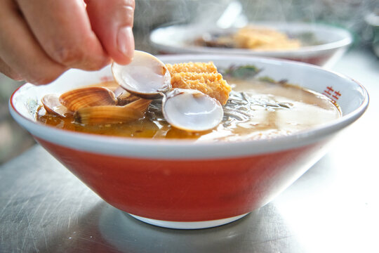 Chef adding mussel on top of hot soup with noodles