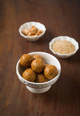 Healthy Til Laddu - balls made with sesame seeds and jaggery in a bowl with raw ingredients.