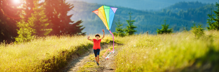 Little happy child boy running with kite. Wonderful mountain landscape in Alps at sunset.