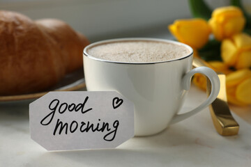 Cup of coffee, croissant and card with phrase GOOD MORNING on white tray, closeup