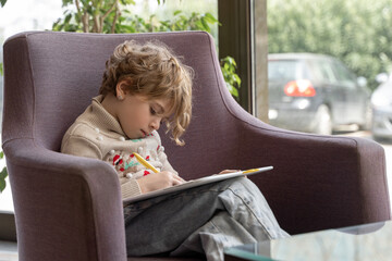 Girl sits in hotel and draws on graphics tablet while traveling with her family