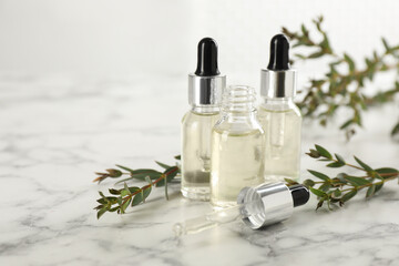 Bottles of eucalyptus essential oil and plant branches on white marble table. Space for text
