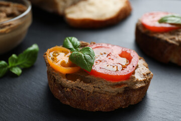 Slice of bread with delicious pate, tomatoes and basil on black table, closeup