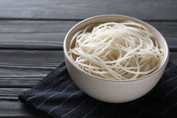 Bowl of tasty cooked rice noodles and napkin on black wooden table, closeup