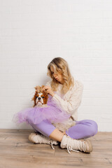 Beautiful woman in beige sweater, purple trousers raising dog ears up spaniel wearing violet...