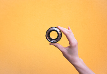 Hand holds a photographic lens on yellow background. - 494661567