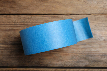 Roll of light blue adhesive tape on wooden background, top view