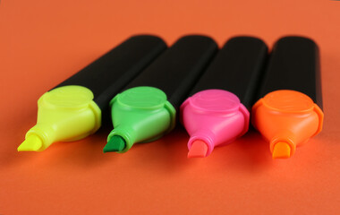 Many colorful markers on orange background, closeup. School stationery