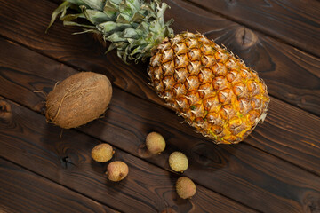 Exotic fruits: pineapple, coconut and lychee on a brown wooden background.