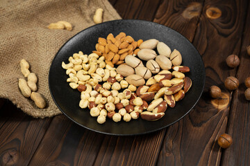 Mixture of nuts in a black plate on a brown wooden background.