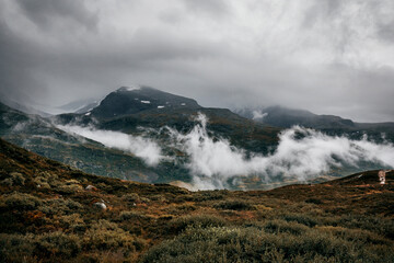 landscape with clouds over the mountains and green field in norway 