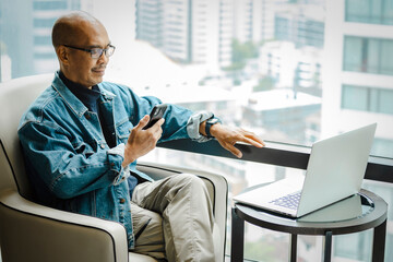 A mature man sitting in an apartment checking stock trading from his smartphone..