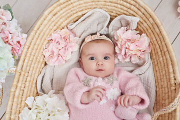 Fototapeta na wymiar Cute baby girl in knitted clothes and wreath with teddy bear toy. Spring background with flowers. Children Protection Day. Mother's day greeting card. International day of happiness
