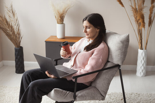 Attractive Confident Woman 30 Years Old Working Remote On Laptop From Cozy Home Sitting In Comfortable Chair With Trendy Interior