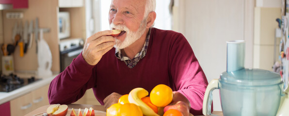 Senior man eating fruit in the kitchen on a sunny day