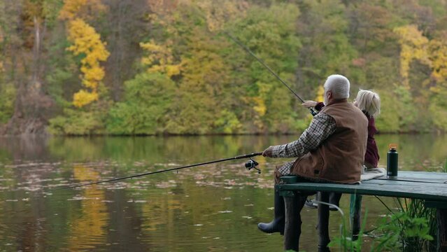 Grandson and grandfather sitting on pier and fishing on lake