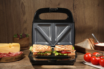 Modern grill maker with sandwiches and different products on wooden table - obrazy, fototapety, plakaty