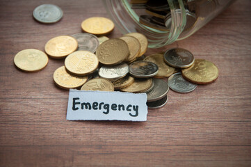 Emergency text on torn paper with jar, coins, and wooden table background.