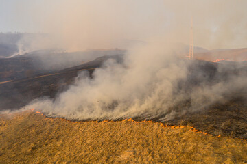 Aerial view of spring dry grass burning field. Fire and smoke in the meadow, nature pollution and danger,common waste are burned